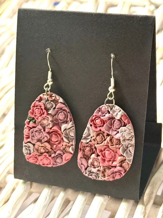 Handmade polymer clay dangle earrings with a stacked floral design in shades of mauve, burgundy, and taupe. The earrings have an organic, textured pattern and are displayed on a black earring card.