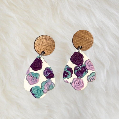 Handmade floral stud earrings with a pink purple and mint green design pressed into a flower mold. The earrings are set on a wooden circle backing.