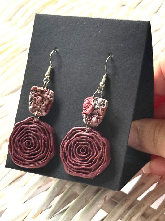 Handmade polymer clay earrings in a spiral design with a textured, layered appearance in a reddish-brown shade. They are displayed on a black earring card.